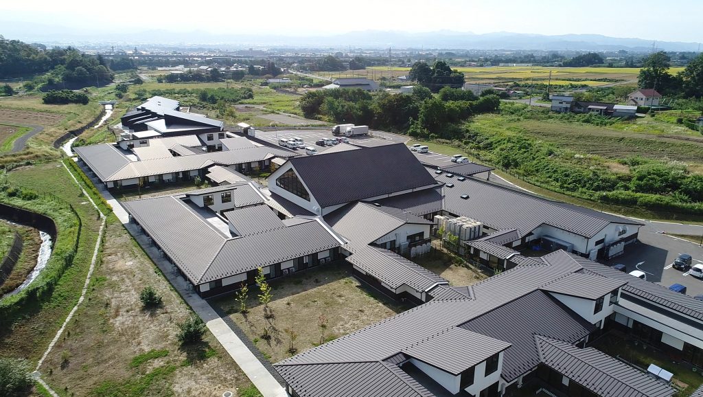 農村地帯に立つ介護施設の全景。複数棟の白と黒の屋根を持つ建物が見える。